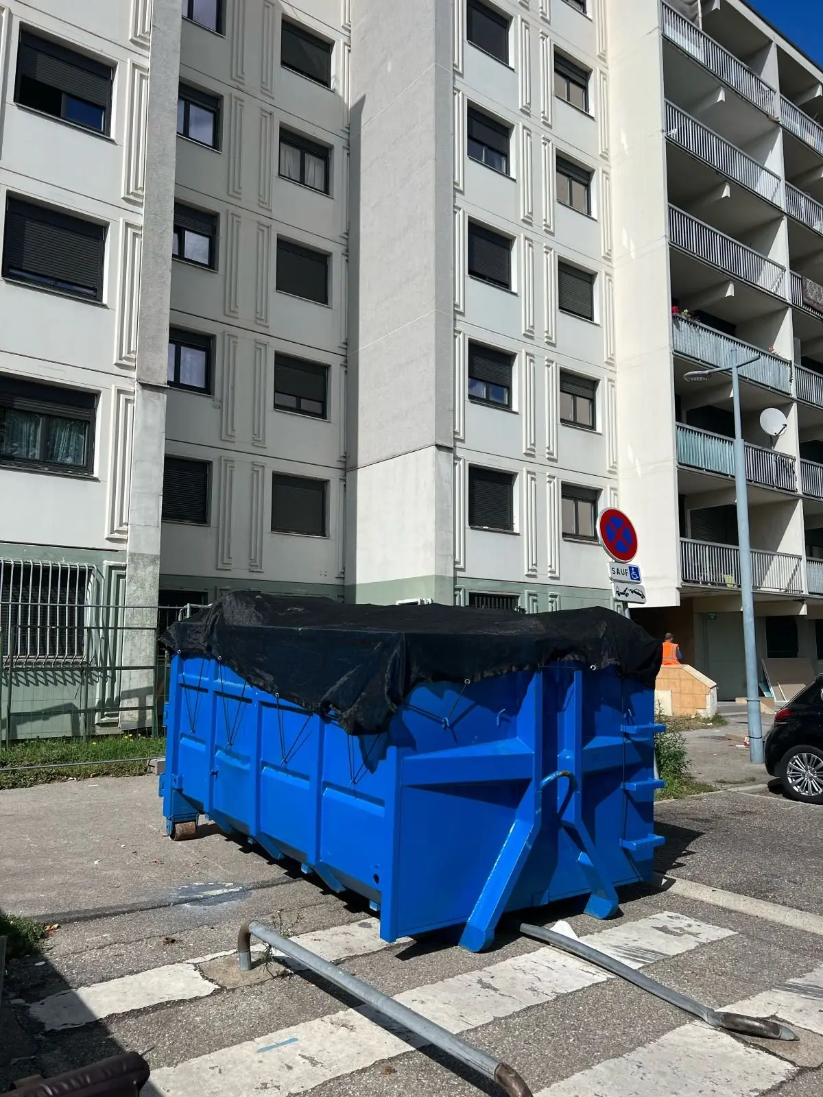 Benne bleue bâchée posée au pied d'un immeuble
