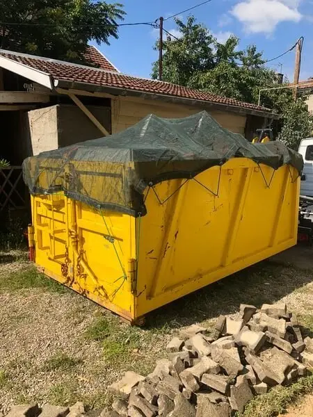 Benne jaune bâchée posée dans un jardin