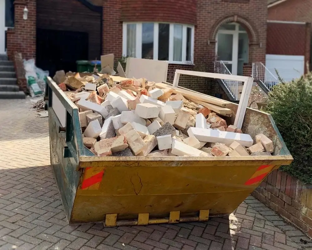 Petite benne jaune remplie de gravats devant une maison